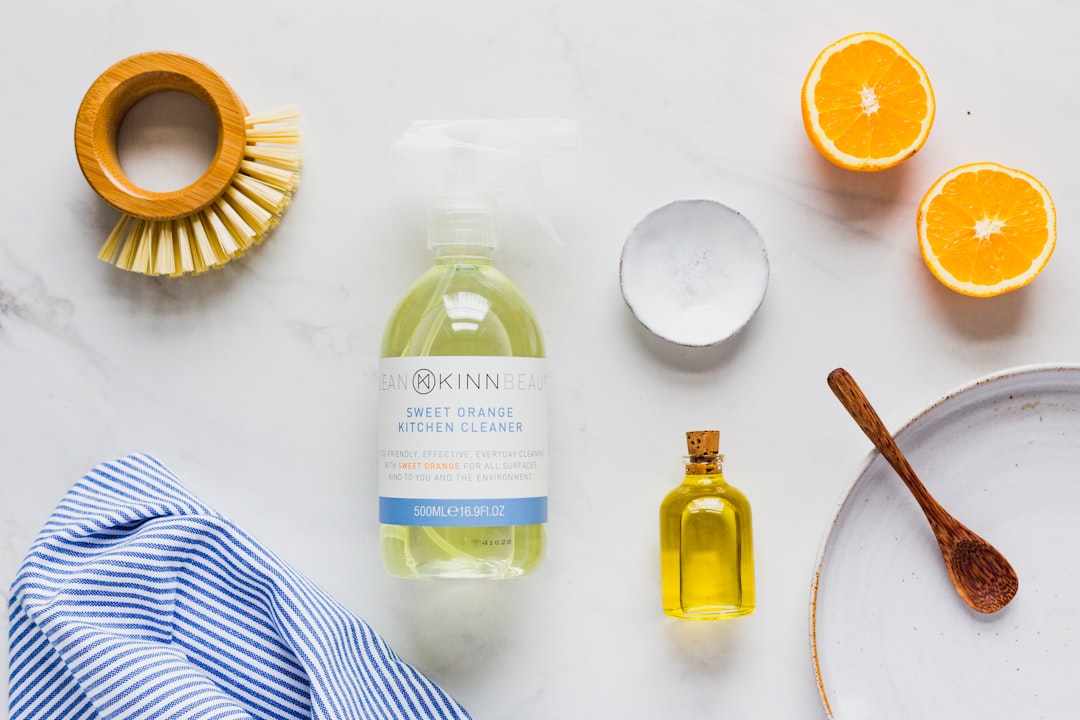 Flat lay of boutique cleaning supplies on a marble surface — natural spray cleaner, wooden brush, sliced oranges, and a striped towel