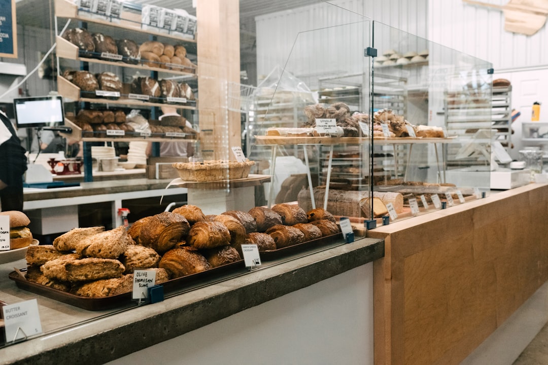 Artisan bakery counter with croissants, pain au chocolat and scones on trays with handwritten labels and shelves of bread behind