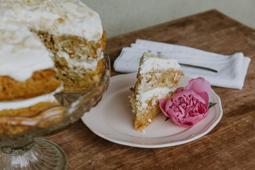 Sliced layer cake on a glass stand with a pink peony garnish on a rustic wooden bakery table