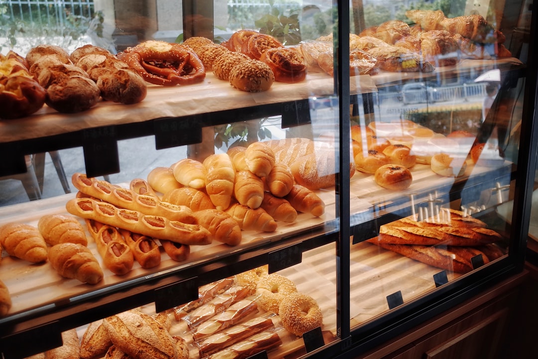 Bakery display case filled with croissants, baguettes, bagels, pretzels and rustic loaves on wooden shelves behind glass