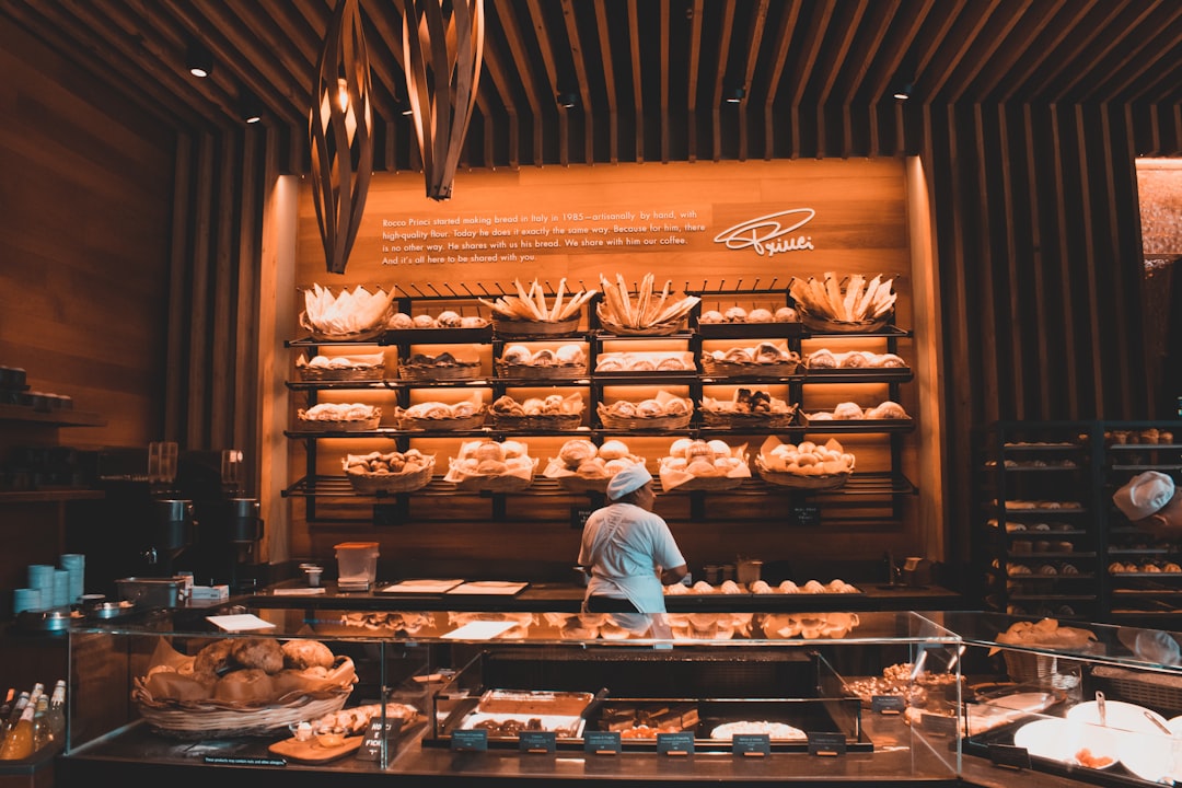 Interior of an artisan retail bakery with rows of wooden shelves displaying breads and pastries behind a glass display case