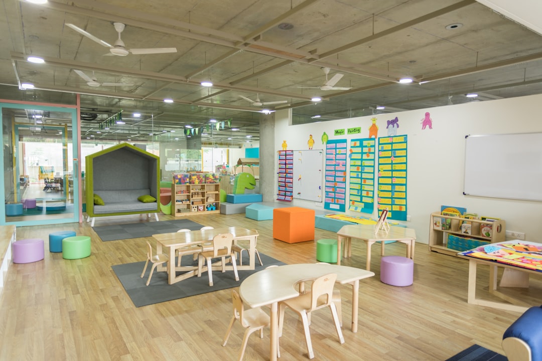 Bright preschool classroom with low wooden chairs, soft seating cubes, exposed concrete ceiling, and a cozy reading nook