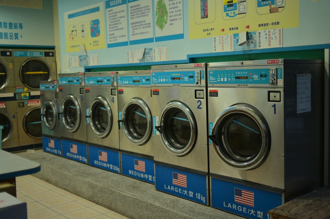 A row of stainless-steel commercial Dexter washers in a bright laundromat, labeled by load size