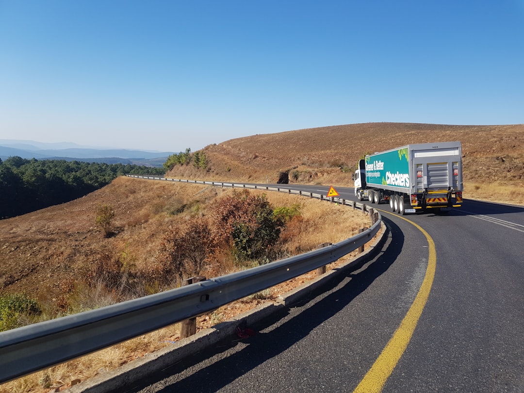 A commercial truck rounding a mountain highway curve with bright blue sky and rolling hills in the distance
