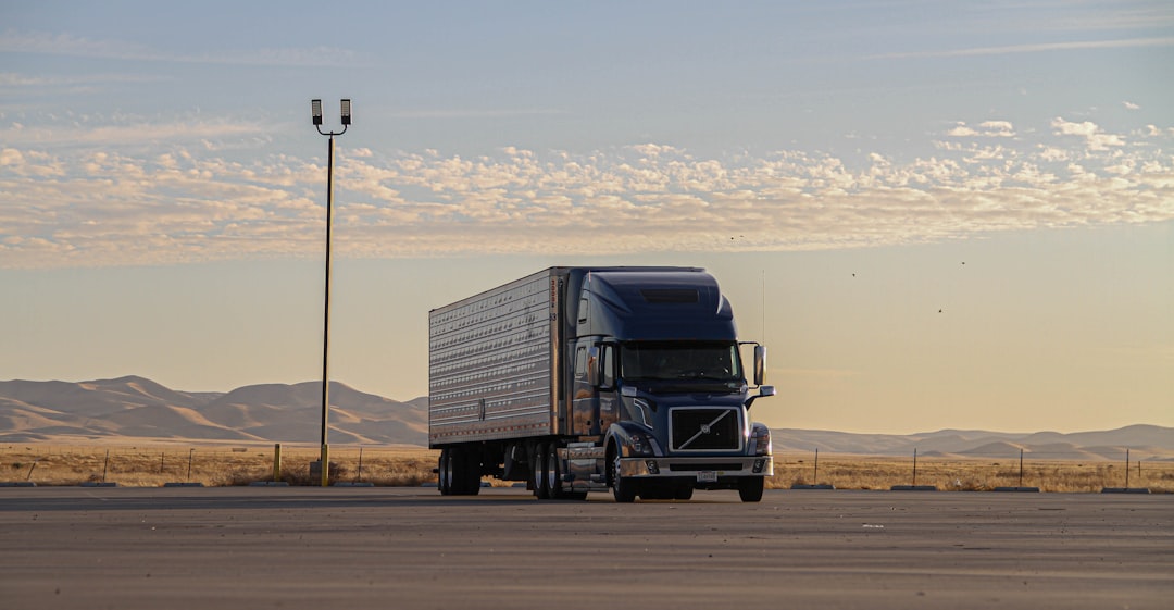 Blue Volvo semi-truck parked in an open lot with distant hills and a partly cloudy sky